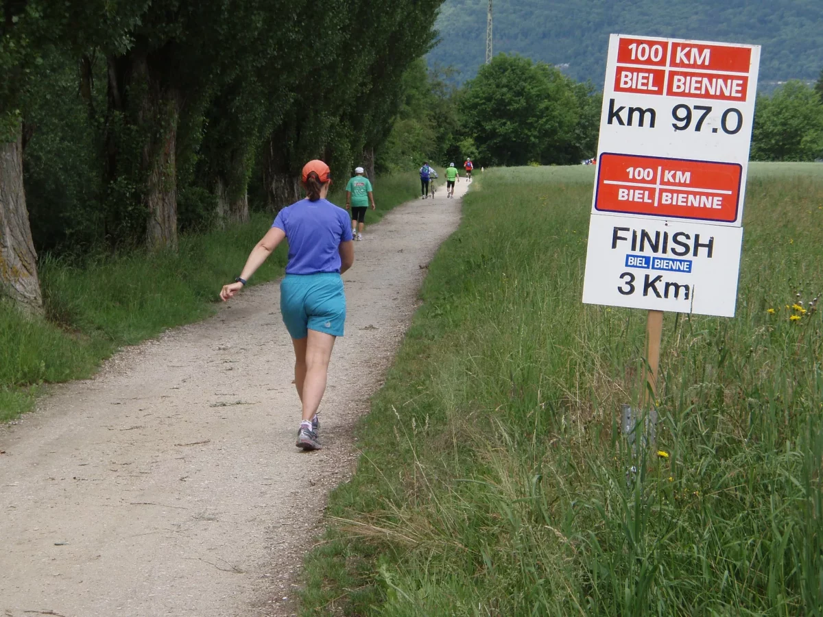 Ultrafutó halad egy földúton a 100 km-es futóverseny 97. kilométerét jelző tábla mellett