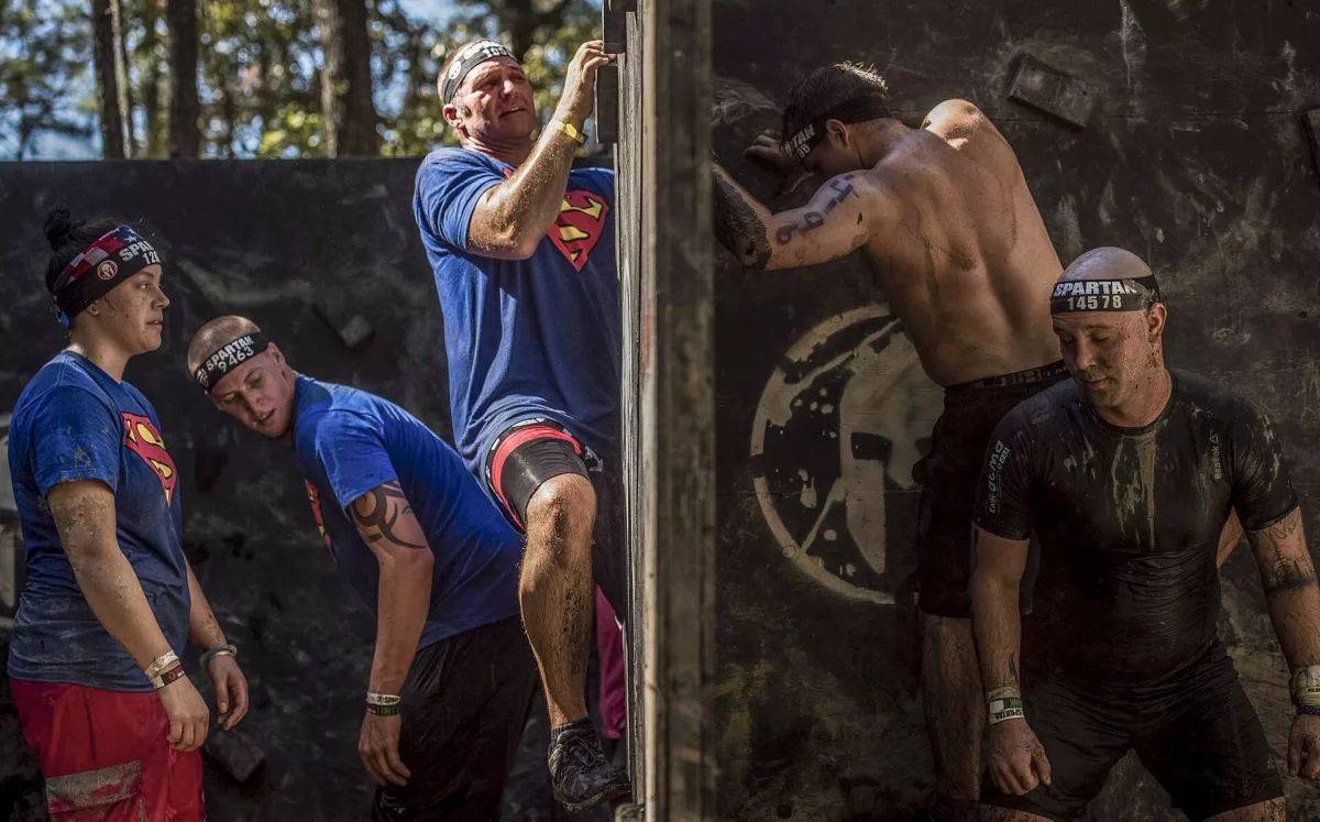 Versenyzők segítik át egymást egy cikcakkos falakadályon egy Spartan Sprint akadályfutó versenyen.